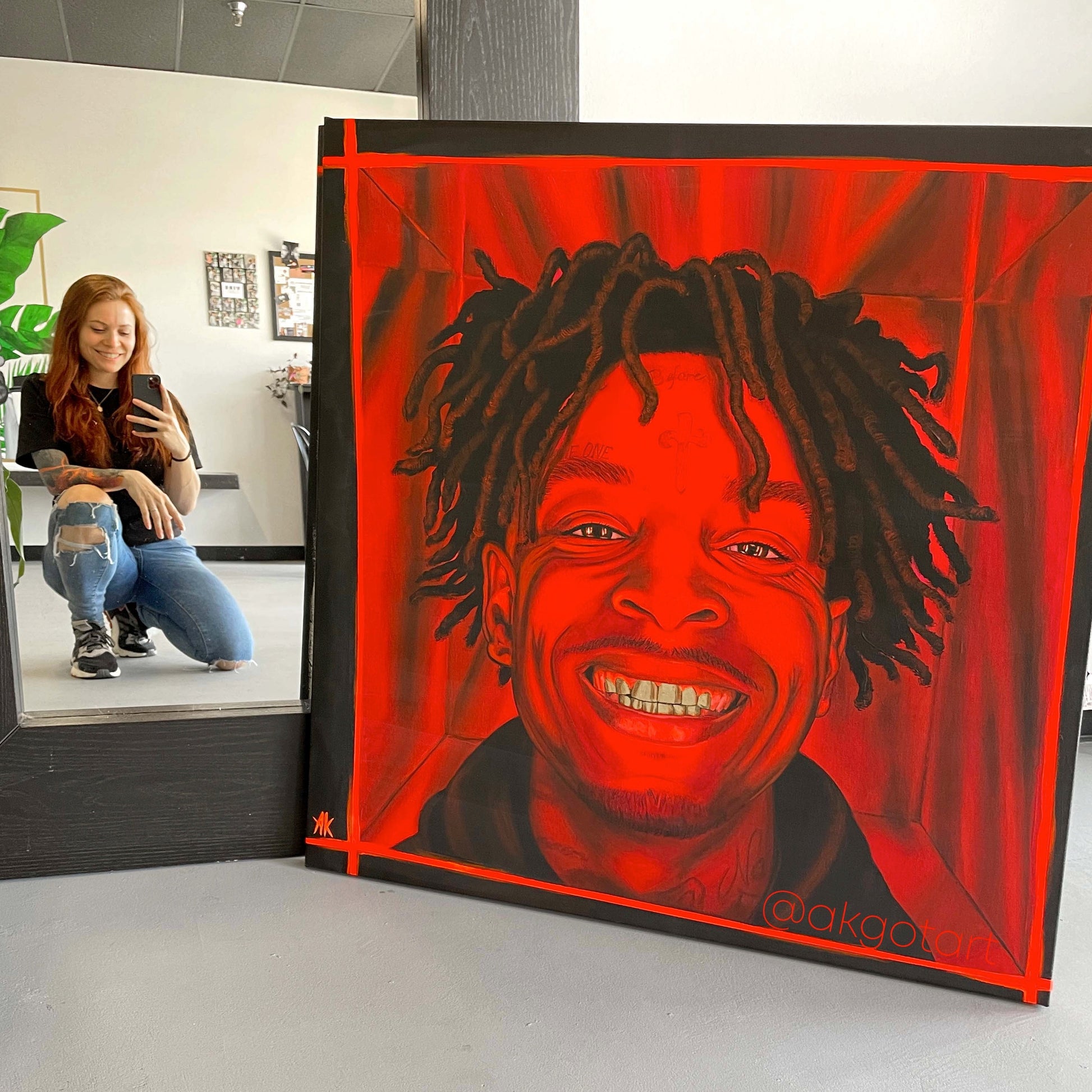 Person taking a photo of a large red and black portrait of rapper 21 savage in an indoor setting